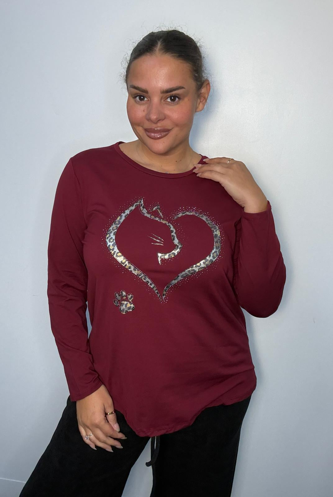 Plus-size model wearing a burgundy long-sleeve top featuring a leopard print heart with cat silhouette, sparkling embellishments and paw print detail.