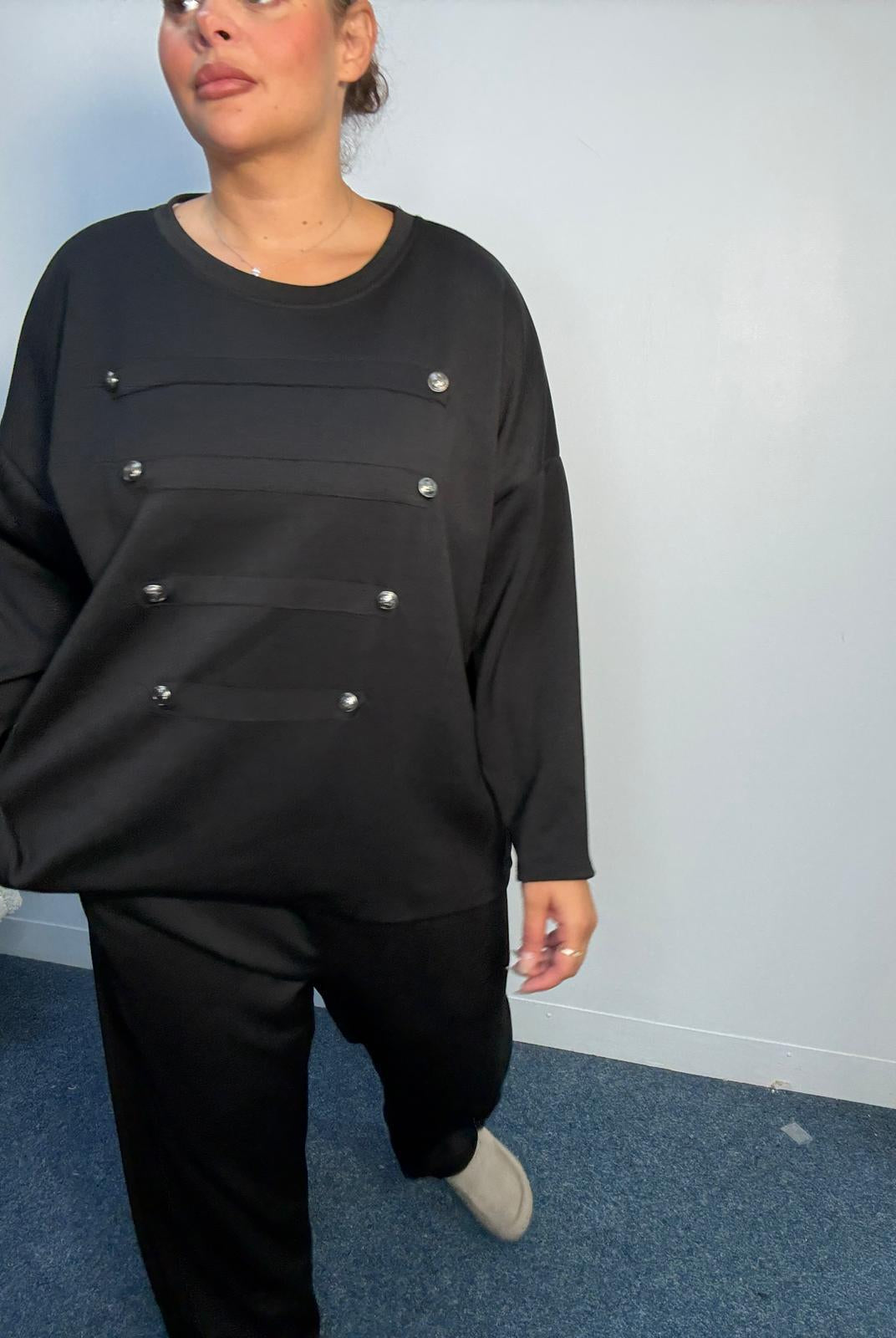 Full-length view of a plus-size black lounge set with decorative horizontal panels, silver-tone buttons and matching straight-leg trousers.