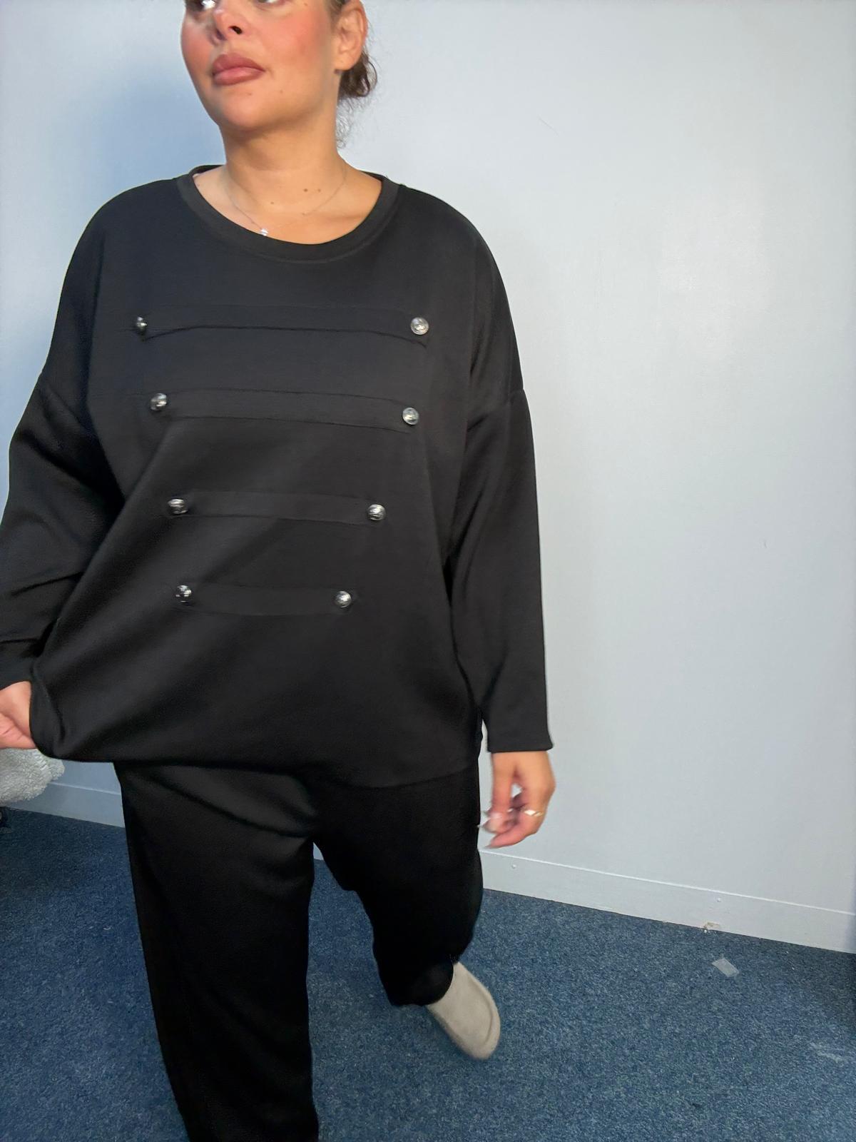 Full-length view of a plus-size black lounge set with decorative horizontal panels, silver-tone buttons and matching straight-leg trousers.