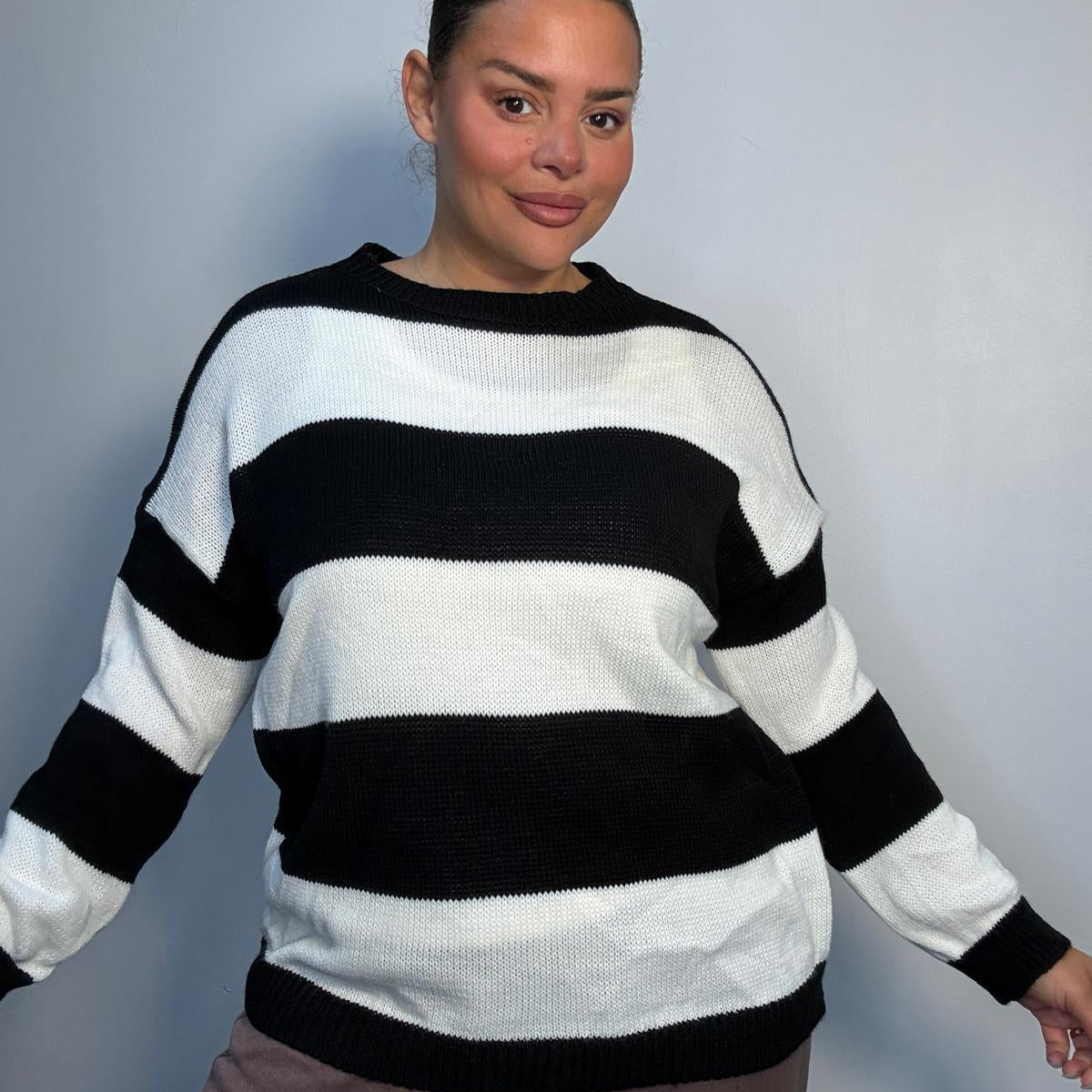 Plus-size model wearing a black and white horizontally striped knitted jumper with round neckline, long sleeves and ribbed trims.