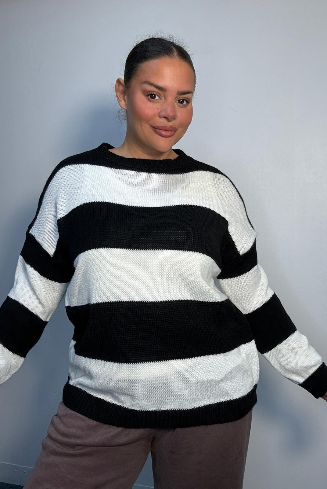 Plus-size model wearing a black and white horizontally striped knitted jumper with round neckline, long sleeves and ribbed trims.