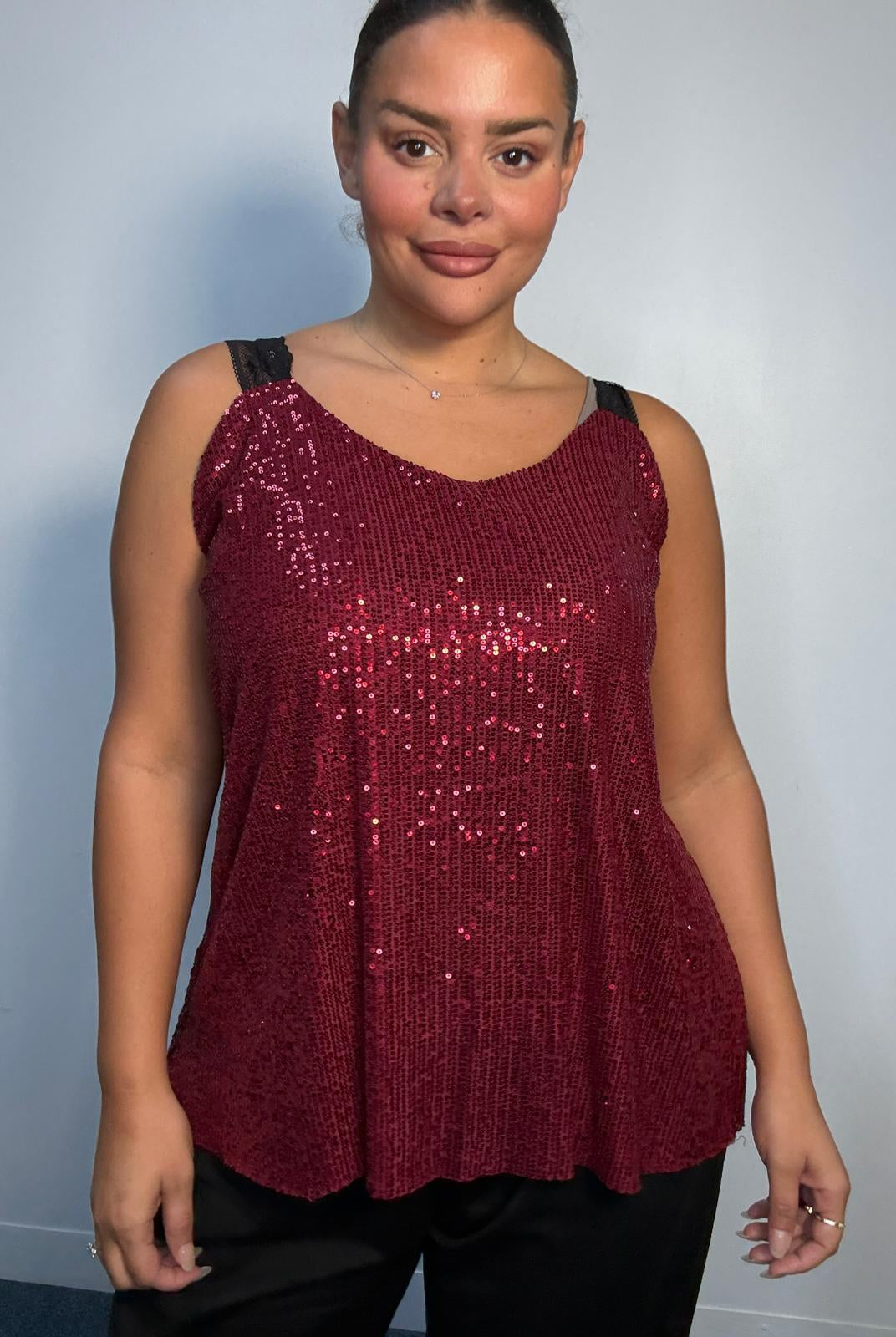 Plus-size model wearing a burgundy sequin cami top with V-neckline, black lace-look shoulder straps and a relaxed flared hem.