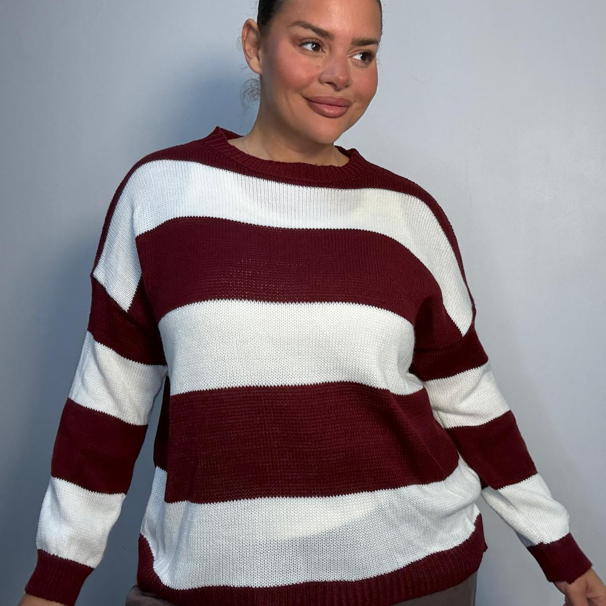 Plus-size model wearing a burgundy and white horizontally striped knitted jumper with round neckline, long sleeves and ribbed trims.