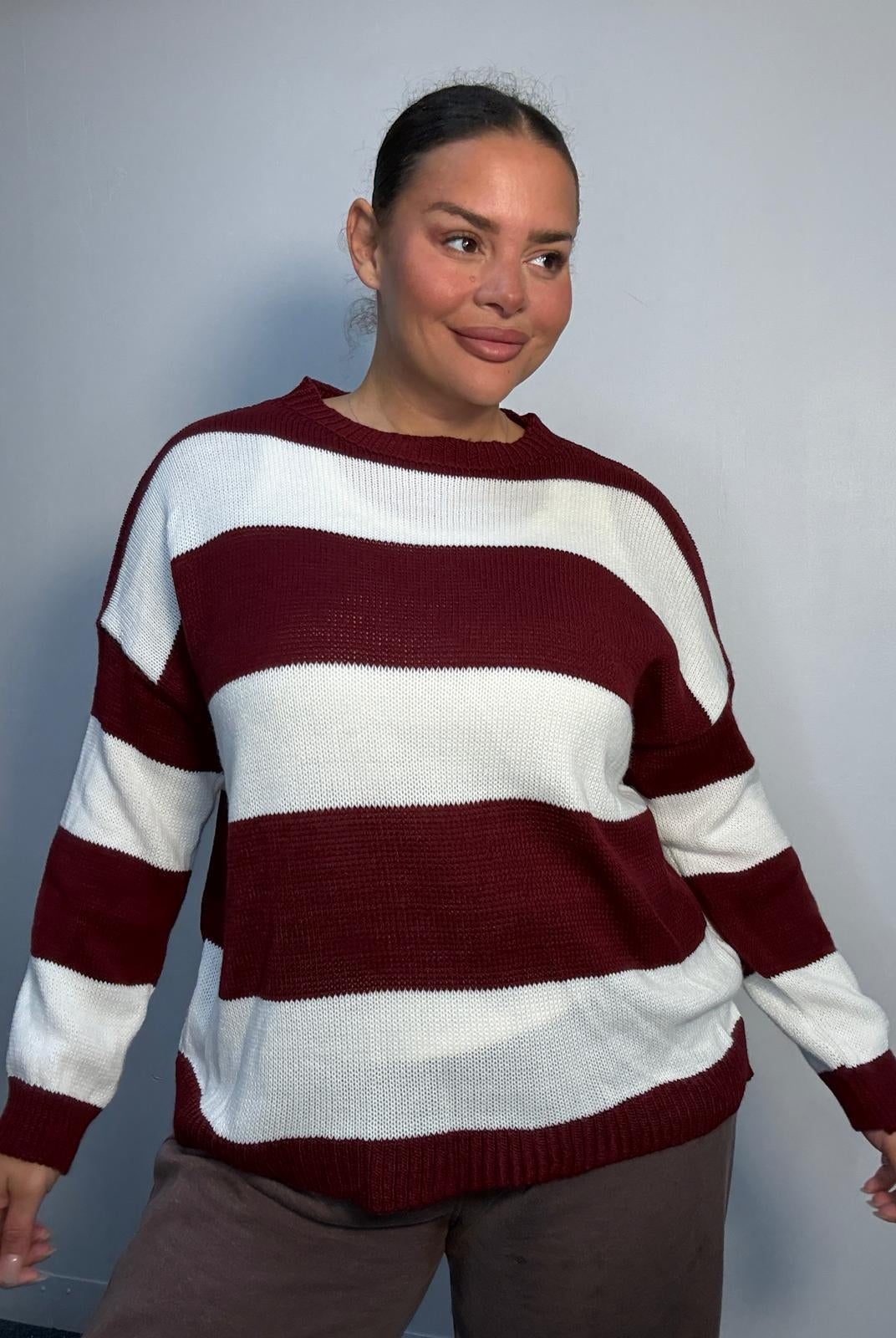 Plus-size model wearing a burgundy and white horizontally striped knitted jumper with round neckline, long sleeves and ribbed trims.