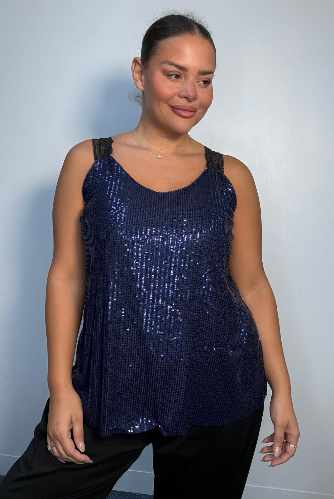 Plus-size model wearing a navy sequin cami top with V-neckline, black lace-look shoulder straps and a relaxed flared hem.