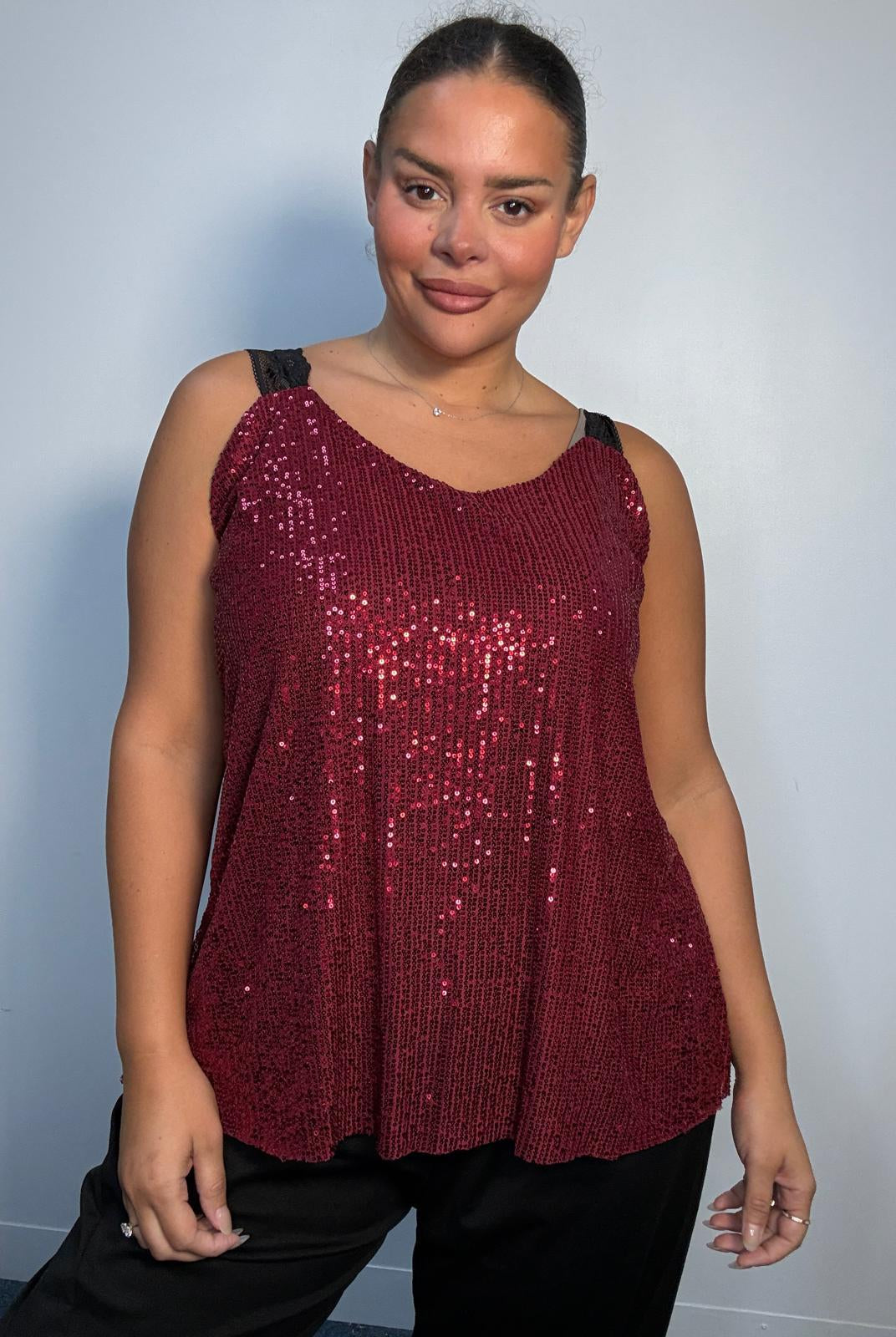 Plus-size model wearing a burgundy sequin cami top with V-neckline, black lace-look shoulder straps and a relaxed flared hem.