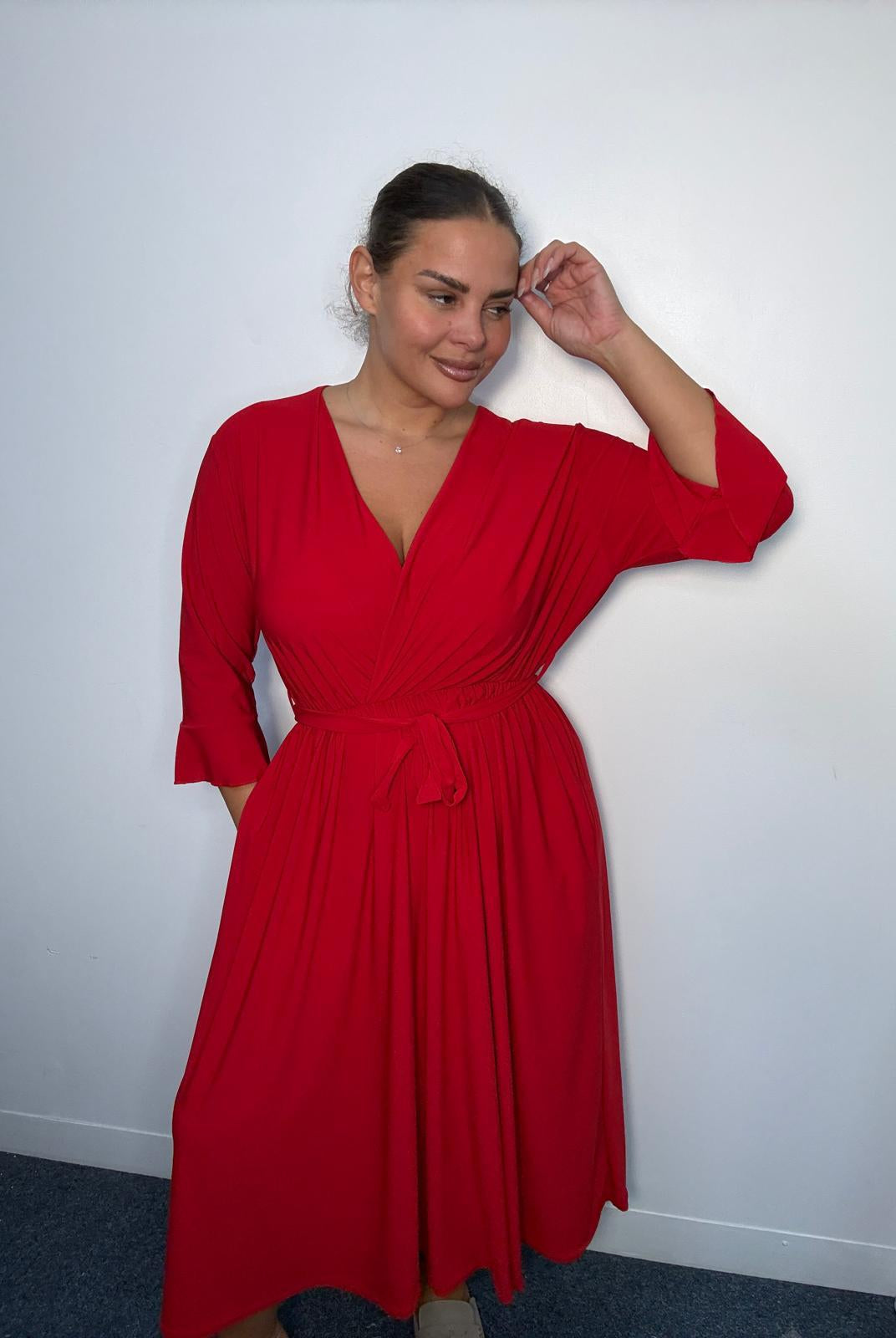 Plus-size model wearing a burgundy wrap-style midi dress with V-neckline, matching tie waist, three-quarter flared sleeves and flowing skirt.
