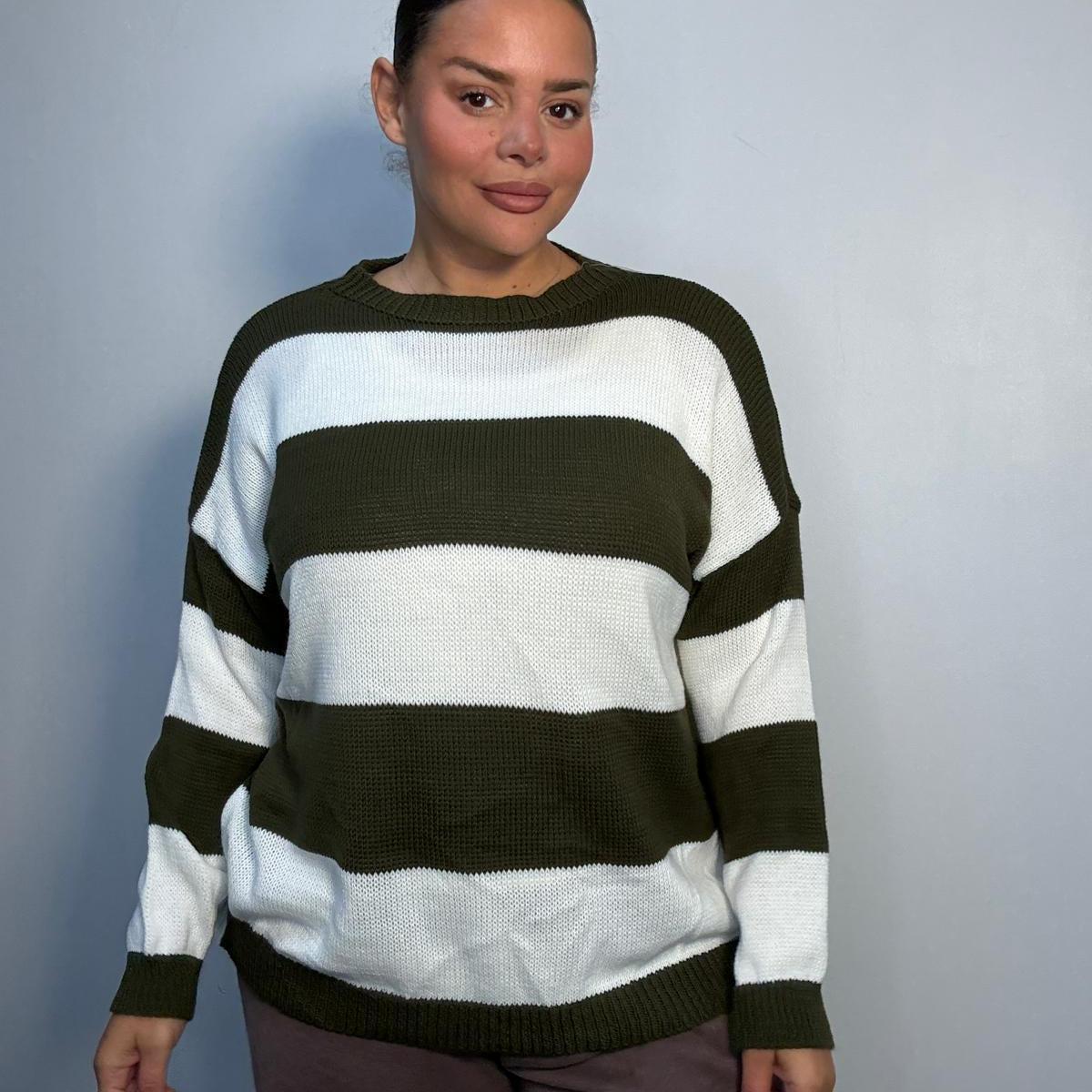 Plus-size model wearing a khaki green and white horizontally striped knitted jumper with round neckline, long sleeves and ribbed trims.