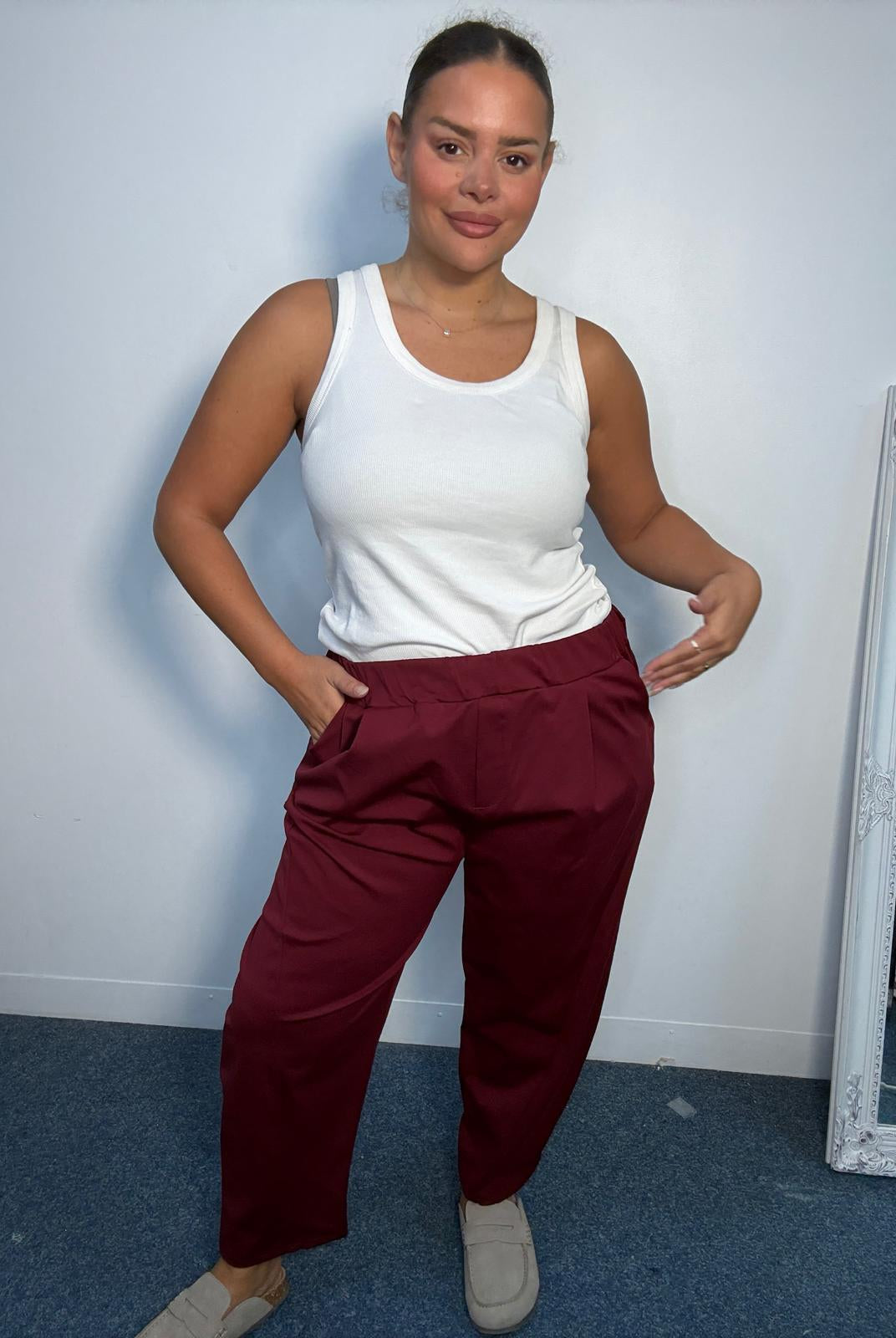 Plus-size model wearing burgundy tapered trousers with an elasticated waistband, front pleat detailing and side pockets.
