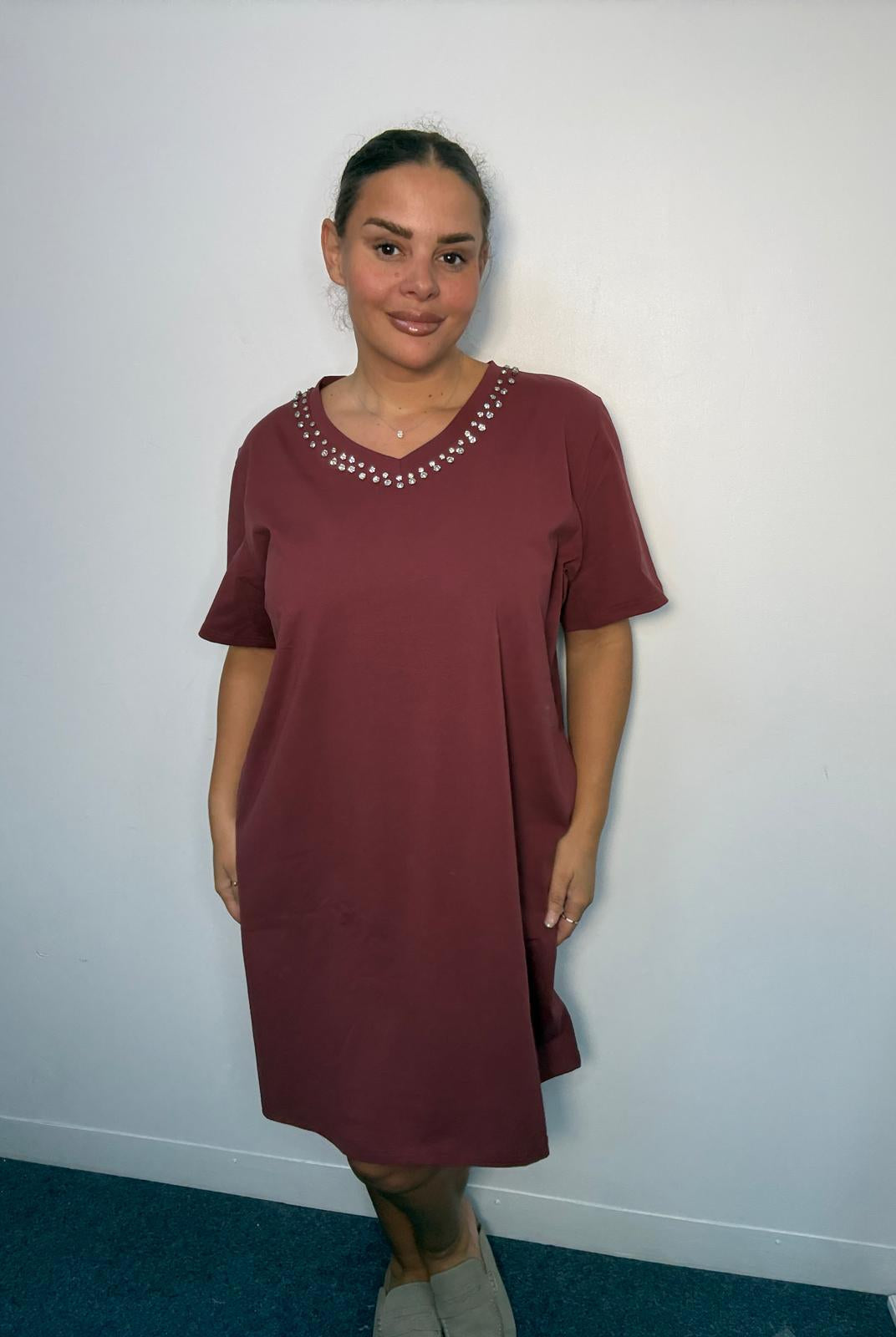 Plus-size model wearing a burgundy V-neck midi dress with sparkling neckline embellishments, short sleeves and relaxed fit.