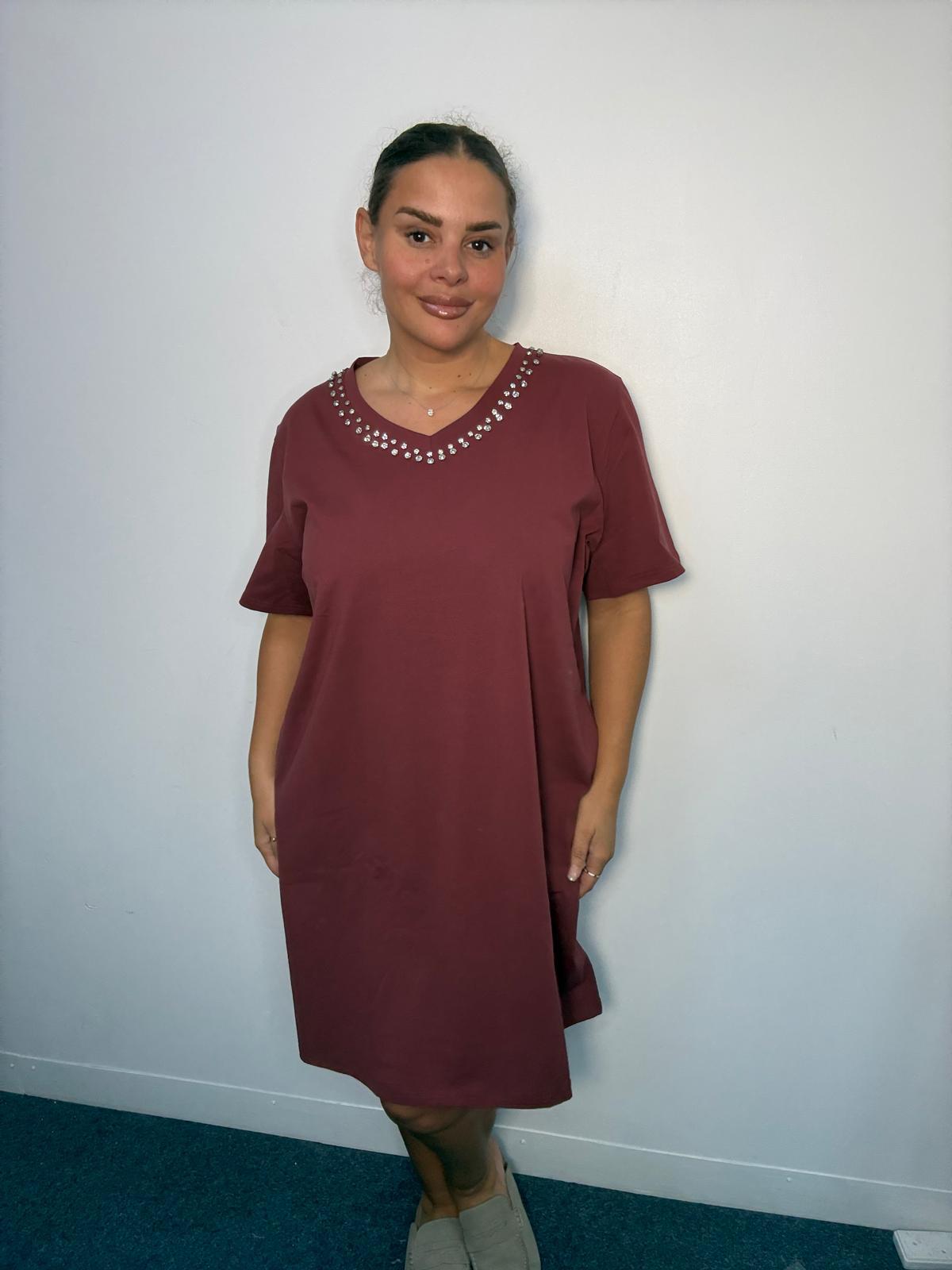 Plus-size model wearing a burgundy V-neck midi dress with sparkling neckline embellishments, short sleeves and relaxed fit.