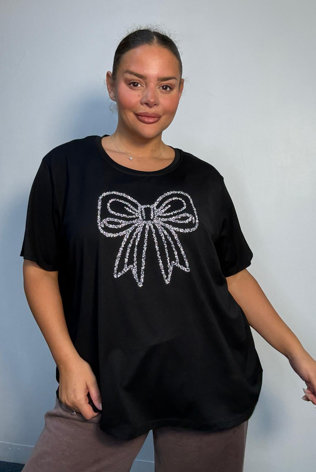 Plus Size Mixed Race Model wearing a black short sleeve top with bow diamante detail at the front