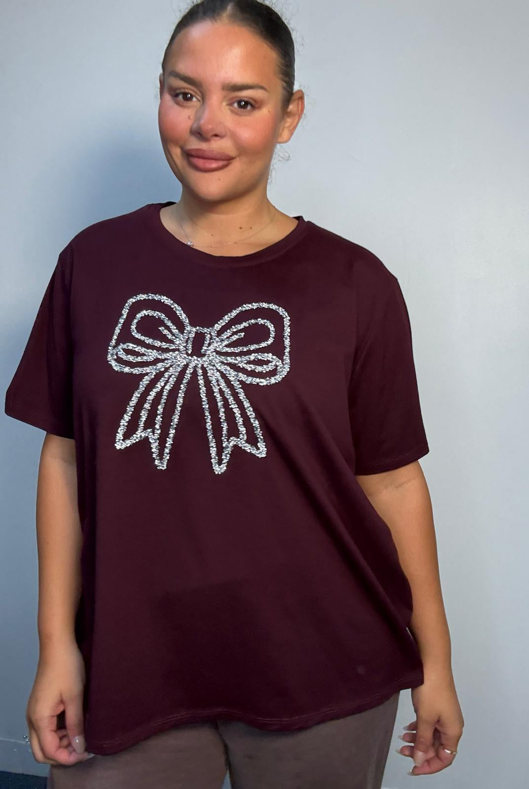 Plus Size Mixed Race Model wearing a burgundy short sleeve top with bow diamante detail at the front