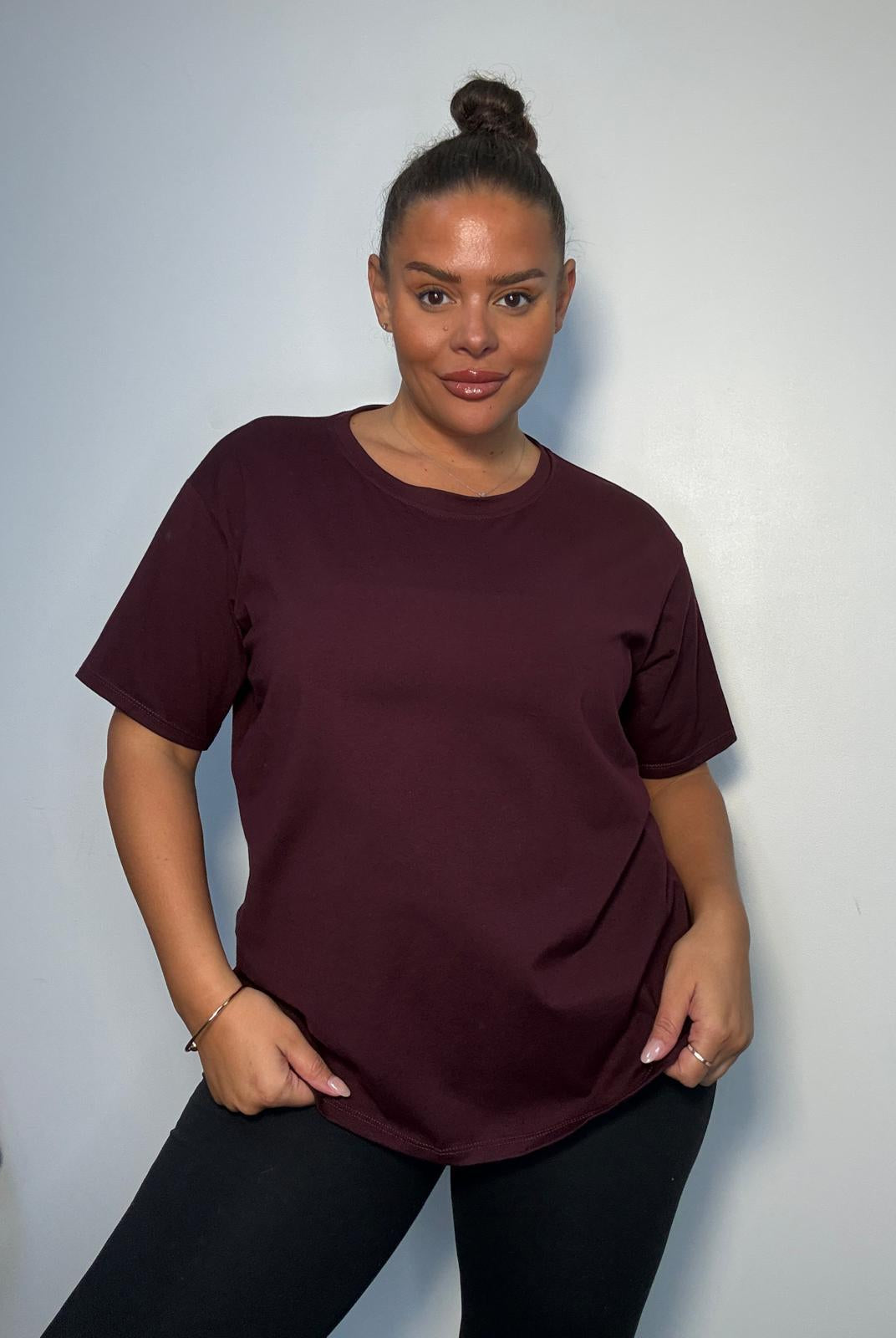 Model wearing a burgundy plus size V-neck T-shirt with short sleeves and a relaxed fit, styled with black trousers.