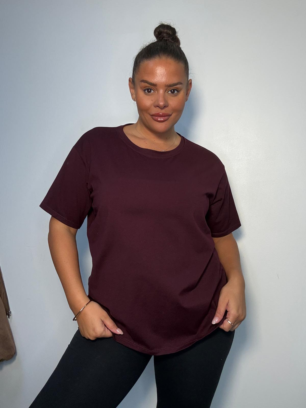 Model wearing a burgundy plus size V-neck T-shirt with short sleeves and a relaxed fit, styled with black trousers.