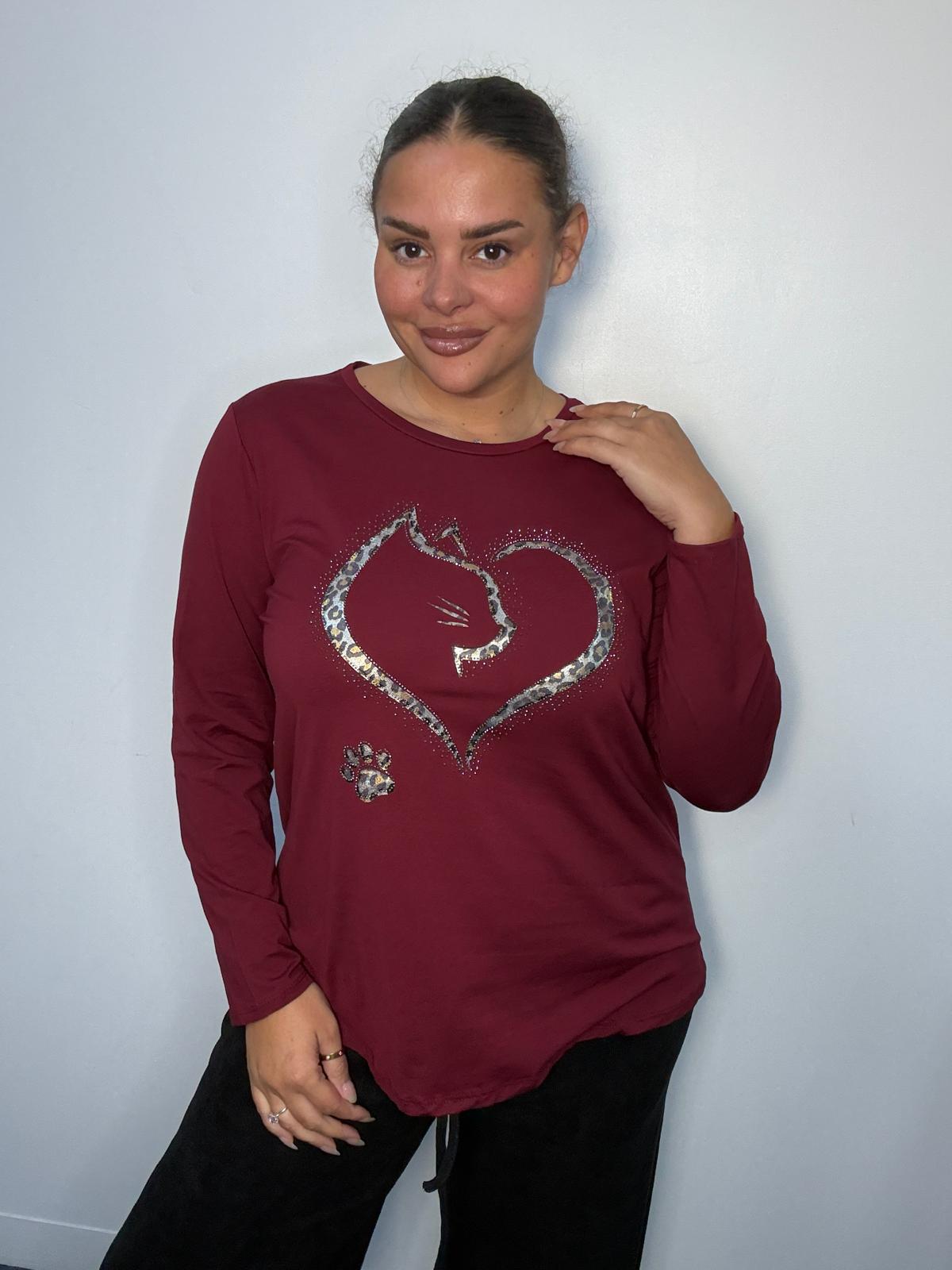 Plus-size model wearing a burgundy long-sleeve top featuring a leopard print heart with cat silhouette, sparkling embellishments and paw print detail.