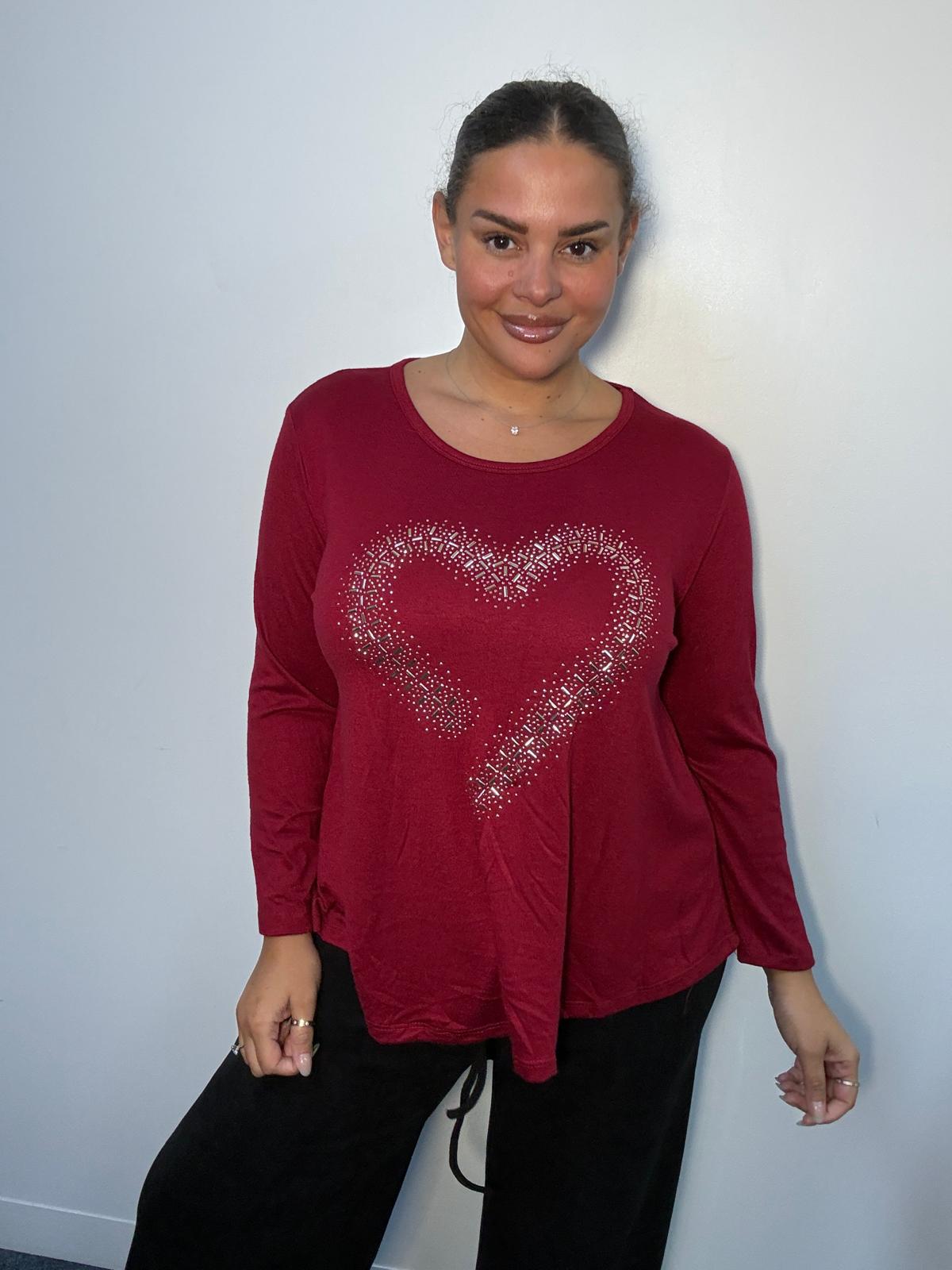 Plus-size model wearing a burgundy long-sleeve top featuring a sparkling diamante-style heart design and asymmetric pointed hem.