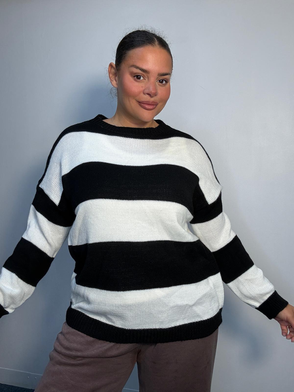 Plus-size model wearing a black and white horizontally striped knitted jumper with round neckline, long sleeves and ribbed trims.