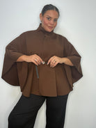 Plus-size model wearing a brown belted cape-style jacket with a high neckline and wide sleeves.