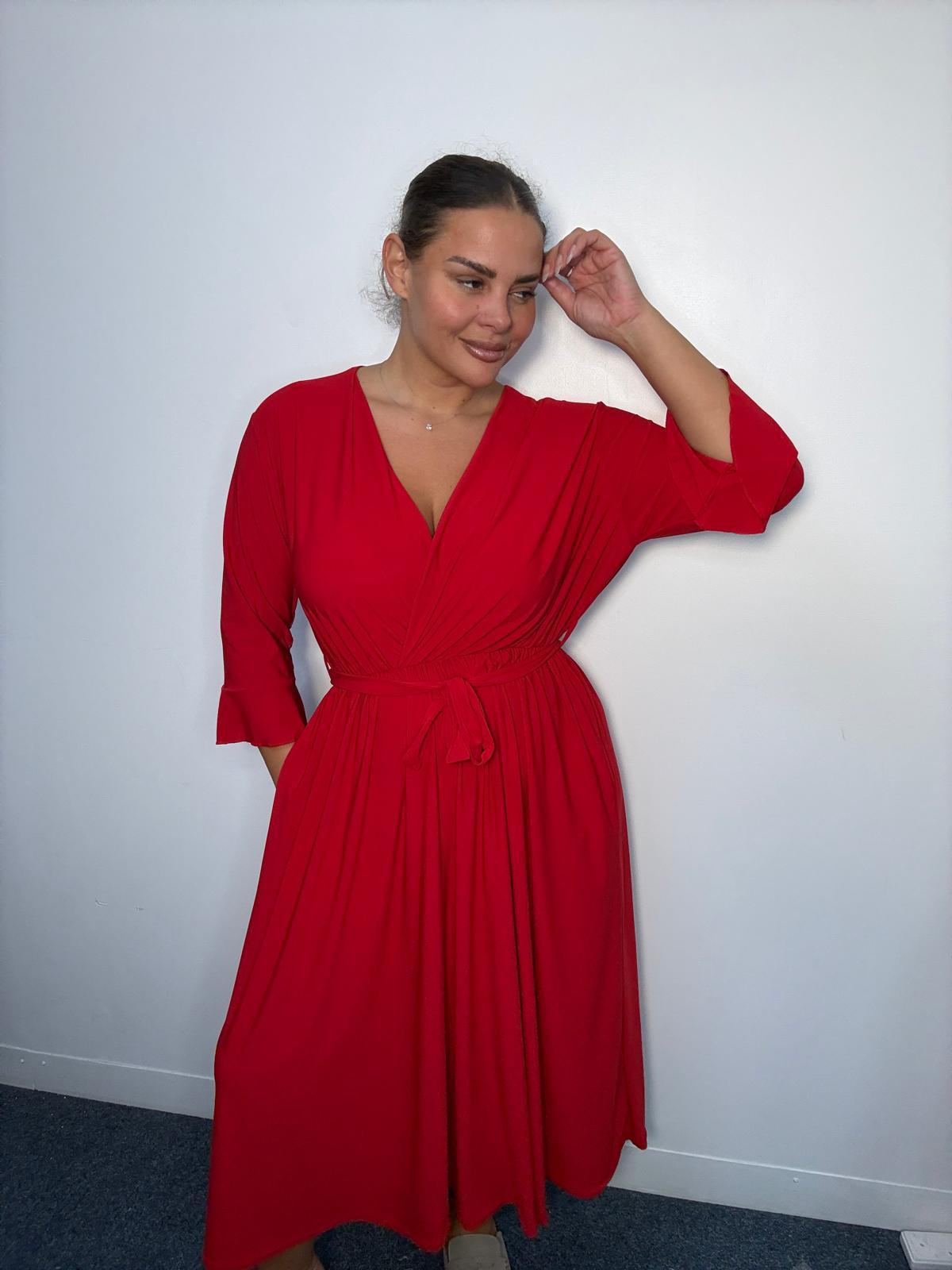 Plus-size model wearing a burgundy wrap-style midi dress with V-neckline, matching tie waist, three-quarter flared sleeves and flowing skirt.