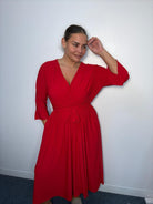 Plus-size model wearing a burgundy wrap-style midi dress with V-neckline, matching tie waist, three-quarter flared sleeves and flowing skirt.