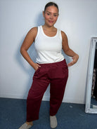Plus-size model wearing burgundy tapered trousers with an elasticated waistband, front pleat detailing and side pockets.
