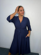 Plus-size model wearing a navy wrap-style midi dress with V-neckline, matching tie waist, three-quarter flared sleeves and flowing skirt.