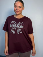 Plus Size Mixed Race Model wearing a burgundy short sleeve top with bow diamante detail at the front
