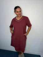 Plus-size model wearing a burgundy midi dress with diamante-style V-neck detailing and hands in the side pockets.
