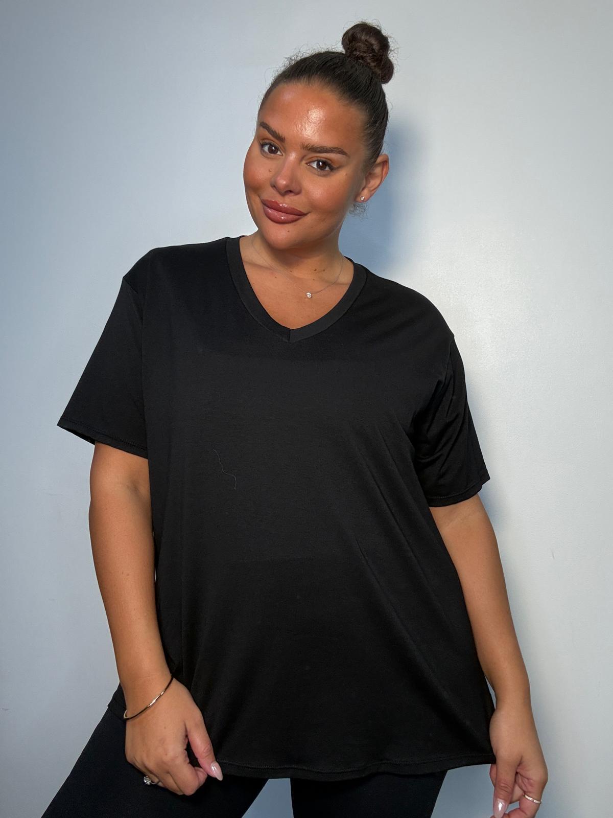 Model wearing a black plus size V-neck T-shirt with short sleeves and a relaxed fit, styled with black trousers.